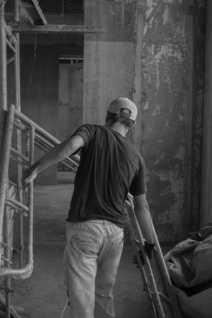 Worker adjusting scaffolding in an industrial indoor setting captured in monochrome.