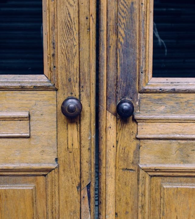Close-up of rustic wooden double doors featuring antique metal knobs and natural weathered textures.