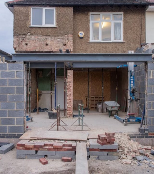 Brick house under renovation with an extension in progress. Visible construction site materials and structure.